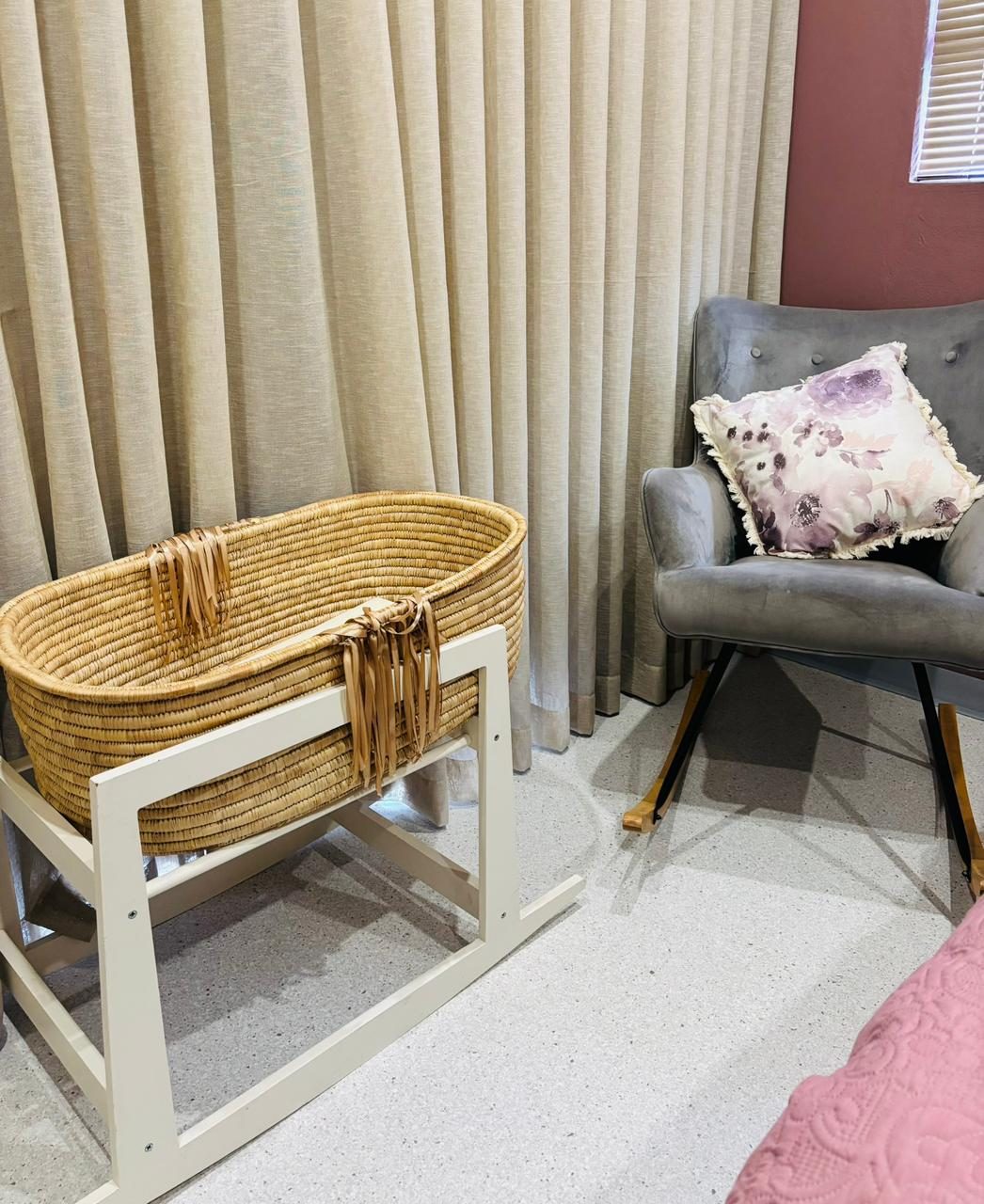 The recovery room: a woven moses basket on a white stand beside a grey rocking chair and linen curtains